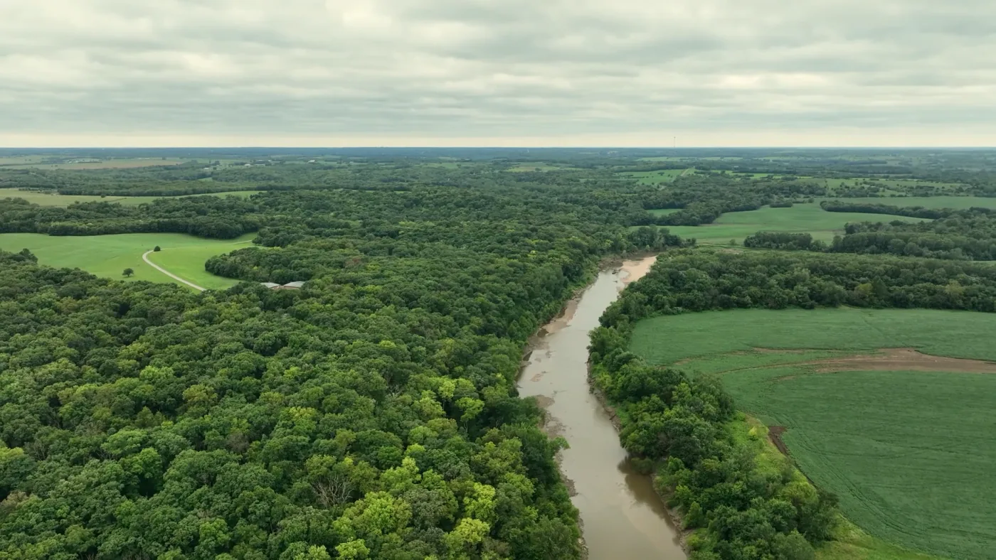 An aerial view of a broad river winding through woodland and green farm fields in Jackson County, Missouri.
